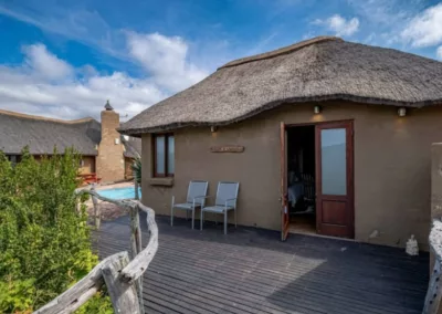 Traditional thatched chalet with a wooden deck and outdoor seating overlooking the natural surroundings at Huntshoek Lodge.